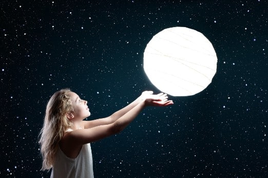 Girl in front of a black background holding up the moon.