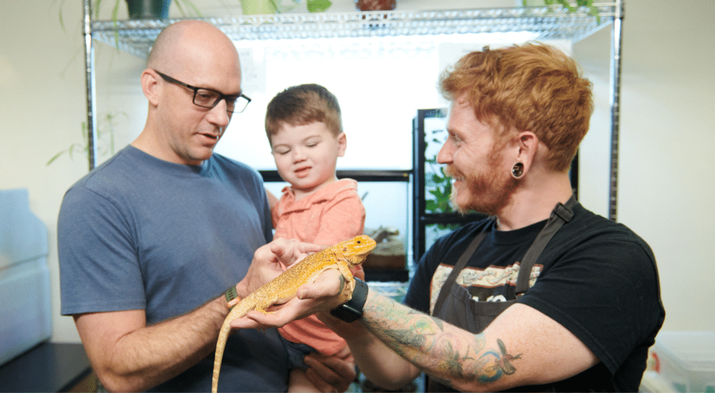 Father holding a child while an omsi educator shows them a lizard